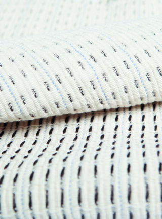 Nahaufnahme eines gefalteten weißen strukturierten Stoffes mit vertikalen schwarzen und blauen Nähten.