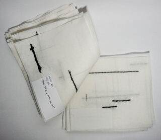 Ein Stapel weißer Stoffmuster mit schwarzen Nähten, ein Muster mit der Aufschrift „106/60 T.King ‚Two or Thirteen‘“.