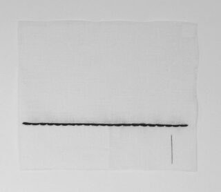 Ein weißes quadratisches Stück Stoff mit einer Reihe kleiner schwarzer Schlaufen am unteren Rand und einer einzelnen vertikalen schwarzen Linie auf der rechten Seite.