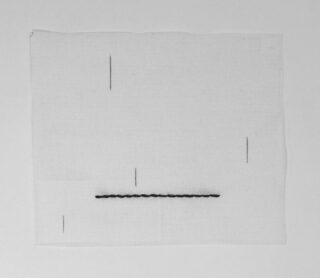 Ein quadratisches Stück weißen Stoffs mit fünf dünnen schwarzen vertikalen Linien und einer dickeren horizontalen schwarzen Nahtlinie.