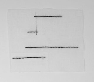 Ein weißes quadratisches Stück Stoff mit mehreren geraden, schwarzen Nählinien unterschiedlicher Länge, die horizontal und vertikal angeordnet sind.