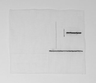 Ein weißes quadratisches Stück Stoff mit drei schwarzen Nähten unterschiedlicher Länge, die nahe der oberen rechten Ecke einen rechten Winkel bilden.