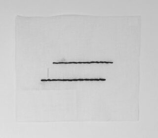 Ein weißes Stoffquadrat mit zwei parallelen horizontalen schwarzen Nählinien und einem schwachen rechteckigen Umriss in der unteren linken Ecke.