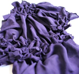 Ein Stück dunkelvioletter Stoff mit gerafften Abschnitten und stoffbezogenen Knöpfen, die in Gruppen auf weißem Hintergrund angeordnet sind.