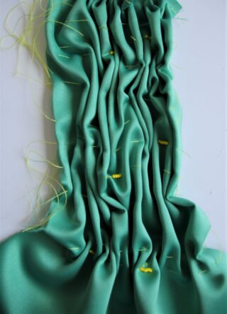 Grüner Stoff ist gerafft und plissiert mit sichtbaren gelben Nähten und losen Fäden auf weißem Hintergrund.