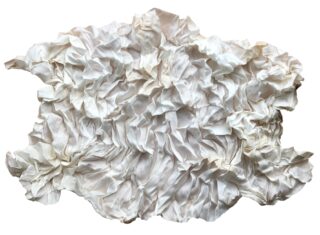 Ein unregelmäßig geformtes Stück weißen Stoffes wird gerafft und zerknüllt, wodurch auf einem schlichten Hintergrund zahlreiche Falten und Knicke entstehen.