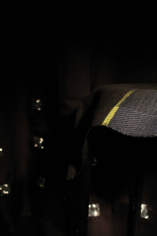 Ein dunkler Raum mit einem schwach beleuchteten schwarzen Stoff, der über eine Oberfläche drapiert ist. Am Rand befindet sich ein einzelner gelber Streifen und im Hintergrund kleine reflektierende Quadrate.