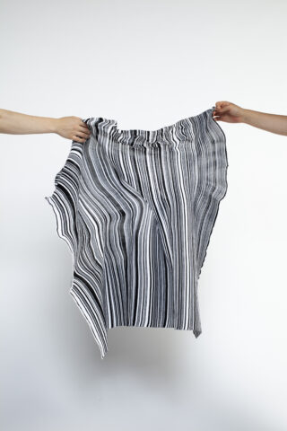 Vor einem schlichten hellen Hintergrund halten zwei Hände ein Stück schwarz-weiß gestreiften Stoff zwischen sich gespannt.