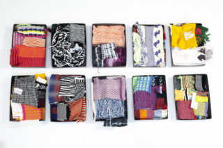 Zehn offene Schachteln mit verschiedenen bunten Stricktextilien, jeweils mit unterschiedlichen Mustern und Texturen, sind in zwei Reihen auf einem weißen Hintergrund angeordnet.