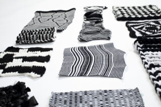 Auf einer weißen Fläche sind mehrere schwarz-weiße Strick- und Webstoffmuster mit unterschiedlichen geometrischen Mustern ausgestellt.