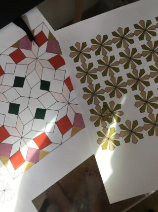 Zwei geometrische Musterzeichnungen auf Papier, eine teilweise mit roten, grünen, rosa und goldenen Formen gefärbt, die andere vollständig mit goldenen und braunen sternförmigen Mustern gefärbt.