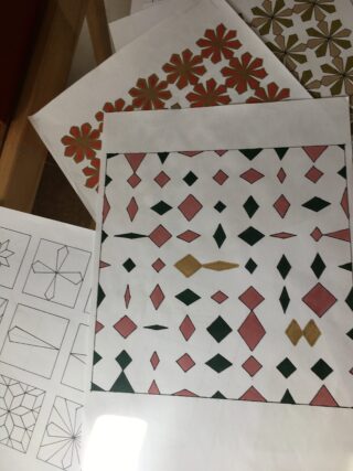 Auf mehreren Blättern Papier sind geometrische Muster ausgebreitet, manche in Farbe, andere mit schwarzen Umrissen.