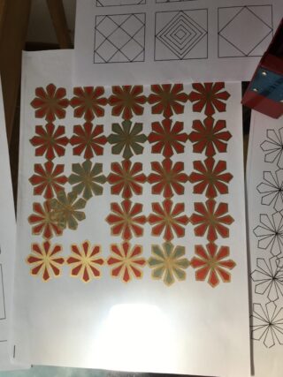 Ein Blatt Papier mit einem Raster aus roten und grünen geometrischen blumenähnlichen Formen, umgeben von anderen Papieren mit schwarz-weißen geometrischen Mustern.