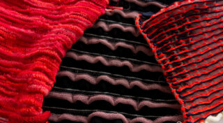 Nahaufnahme von mehrlagigen Textilien mit wellenförmigen Mustern in Rot, Rosa und Schwarz, die die Texturen und Nähdetails des Stoffes hervorheben.