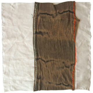 Ein Stück gemusterter brauner Stoff mit sichtbaren weißen und orangefarbenen handgenähten Nähten ist auf einem größeren weißen Stoffhintergrund platziert.