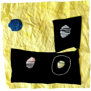 Ein gelbes Stoffquadrat mit zwei schwarzen Stoffflicken, die jeweils weiß gestickte Ovale aufweisen, und einem blauen gestickten Oval direkt auf dem gelben Stoff.