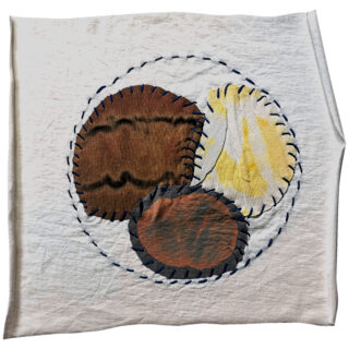 Ein weißes Tuch weist drei überlappende, unregelmäßig geformte Stoffstücke in Braun, Gelb und Grau auf, die mit blauen Nähten in einem kreisförmigen Muster umrandet sind.