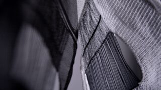 Nahaufnahme von abstrakt strukturierten Stoff- und Netzmaterialien in Grautönen, die Muster und Schichten mit Licht und Schatten zeigen.