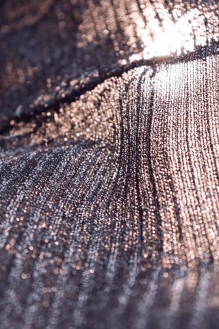 Nahaufnahme einer strukturierten, schimmernden Stoffoberfläche, die Licht reflektiert und ein Muster aus hellen und schattigen Bereichen erzeugt.