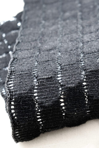 Nahaufnahme eines gefalteten Stücks schwarzen, locker gewebten Stoffes mit einem gitterartigen Muster und sichtbaren Lücken zwischen den Fäden.