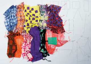 Neun bunte, gemusterte Stoffstücke werden auf einer weißen Oberfläche präsentiert, im Hintergrund sind mit Bleistift gezeichnete Diagramme und Skizzen zu sehen.