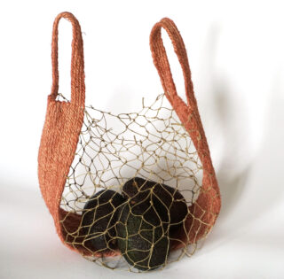 Ein handgefertigter Korb mit strukturierten orangefarbenen Seiten und einem Drahtgeflechtboden enthält drei glatte dunkle Steine vor einem schlichten weißen Hintergrund.