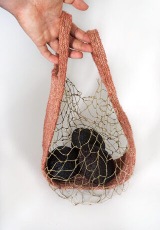 Eine Hand hält einen rosa gewebten Netzbeutel mit mehreren Avocados vor einem schlichten weißen Hintergrund.