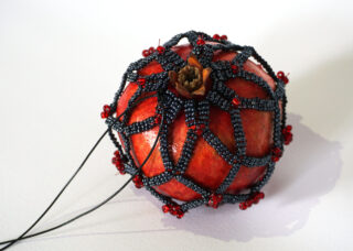 Auf einer weißen Oberfläche liegt ein Granatapfel, der mit einem schwarz-roten Perlennetz bedeckt ist.