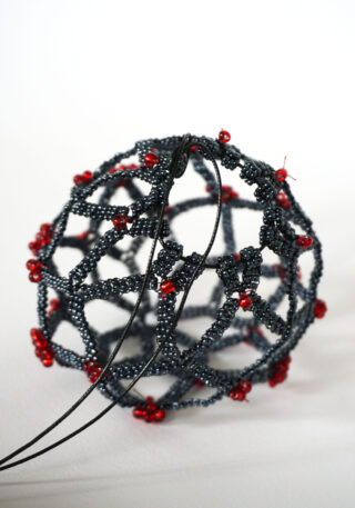Ein kugelförmiges geometrisches Perlenornament aus kleinen schwarzen Perlen, akzentuiert mit Ansammlungen roter Perlen und mit einer schwarzen Kordel zum Aufhängen.