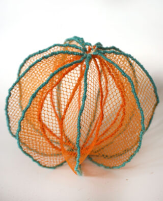 Ein weißes Objekt ist in ein orangefarbenes und blaugrünes Netz eingewickelt, wodurch vor einem weißen Hintergrund eine segmentierte Kugelform entsteht.