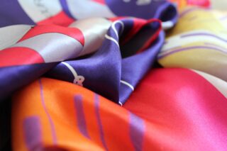 Nahaufnahme eines farbenfrohen, seidigen Stoffes mit glatter Textur und lebendigen Mustern in Lila-, Orange-, Rot- und Gelbtönen.