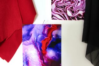 Ein Foto zeigt zwei abstrakte Gemälde mit wirbelnden Farben, links ein Stück roten Stoff und rechts ein schwarzes Netzgewebe, alle auf einer weißen Oberfläche angeordnet.