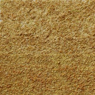 Eine Nahaufnahme einer großen Menge getrockneten, zerkleinerten gelblich-grünen Pflanzenmaterials, das gleichmäßig über die Oberfläche verteilt ist.