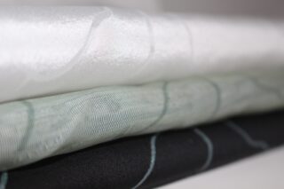 Drei ordentlich gefaltete Stoffstücke in Weiß, Hellgrau und Schwarz, jedes mit einem dezenten, wellenförmigen Linienmuster.