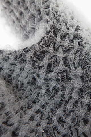 Nahaufnahme eines strukturierten, grauen Netzgewebes mit einem wellenförmigen, geschichteten Muster und komplizierten Details.