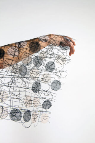 Eine mit einem transparenten Stoff bedeckte Hand mit abstrakten schwarzen Linien und grauen kreisförmigen Formen vor einem schlichten weißen Hintergrund.