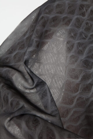 Nahaufnahme eines dunklen, halbtransparenten Stoffes mit einem strukturierten, wellenförmigen Muster und sichtbaren Falten.