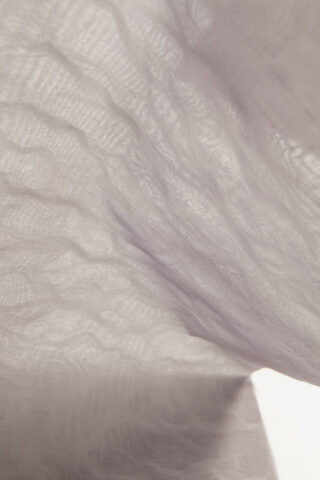 Nahaufnahme eines leichten, halbtransparenten Stoffes mit weichen Falten und knittriger Textur, beleuchtet durch diffuses Licht.