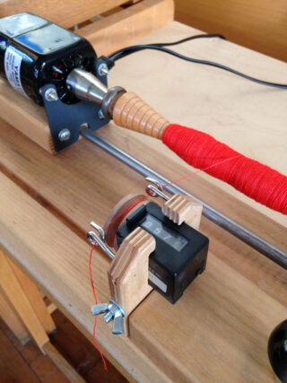 Ein Garnwickler aus Holz mit einem angebrachten mechanischen Zähler verfolgt die Menge des roten Garns, das auf die Spule gewickelt wird.