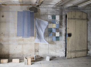 Verschiedene Stoffe in blau und grau, aufgehängt in einem Kellerraum.