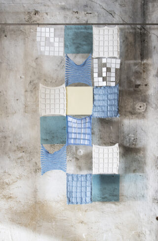 Verschiedene Stoffe in blau und grau, aufgehängt vor einer grob verputzen Wand.