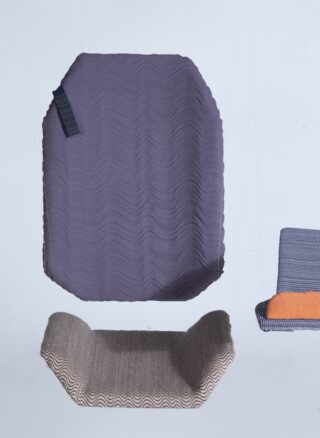 Drei Stoffbahnen in unterschiedlichen Farben und Texturen sind an dünnen Drähten vor einem hellen Hintergrund aufgehängt.