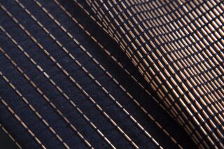 Nahaufnahme eines dunklen Stoffes mit parallelen, diagonal verlaufenden goldmetallischen Streifen, die ein strukturiertes geometrisches Muster erzeugen.