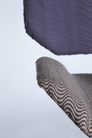 Nahaufnahme von zwei überlappenden strukturierten Stoffen; der obere Stoff ist lila und der untere Stoff ist grau mit einem wellenförmigen Streifenmuster.