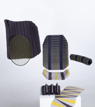 Ein Satz Textilstücke mit geometrischen Mustern in Schwarz, Gelb, Grau und Weiß, präsentiert vor einem schlichten weißen Hintergrund auf und über einem weißen Sockel.