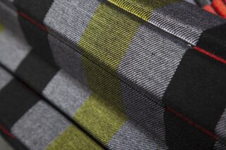 Nahaufnahme eines gefalteten Stoffes mit einem geometrischen Muster aus schwarzen, grauen, gelben und grünen Rechtecken mit feinen diagonalen Linien.