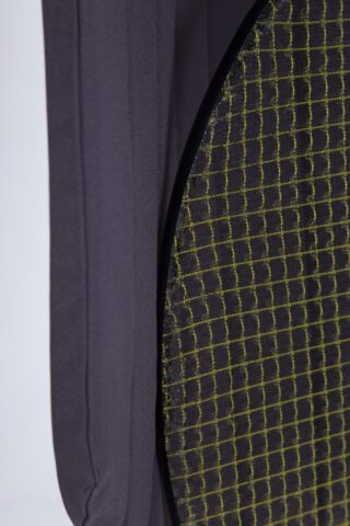 Nahaufnahme eines dunkelgrauen Stoffes neben einem runden Objekt, das mit einem schwarzen Netz bedeckt ist, das ein gelbes Gittermuster aufweist.