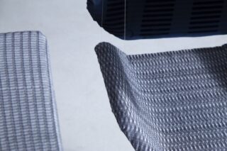 Nahaufnahme von zwei strukturierten, grauen Stoffoberflächen und einem Teil eines dunklen Objekts, die alle über einem hellen Hintergrund schweben.