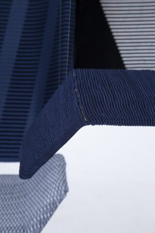 Nahaufnahme von mehrlagigen Textilien in Marine- und Grautönen, die gerippte und gestreifte Muster mit sichtbaren Nähten und strukturierten Oberflächen zeigen.