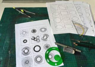 Ein Schreibtisch mit geometrischen Zeichenwerkzeugen, Bleistiften und Papier mit verschiedenen geometrischen Skizzen und Mustern im Spirograph-Stil.